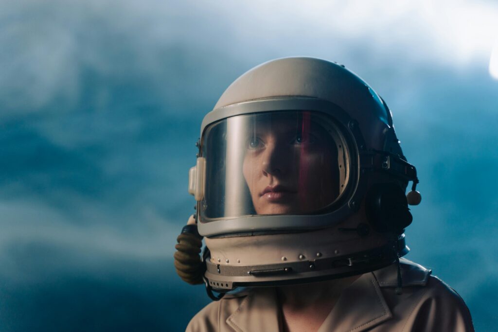 A woman wearing a space helmet with a blue sky background.